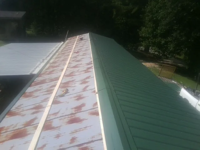 Old rusted panels beside newly installed green metal roofing — Wind Damage Roof Repair by Roofing Brothers in Jacksonboro
