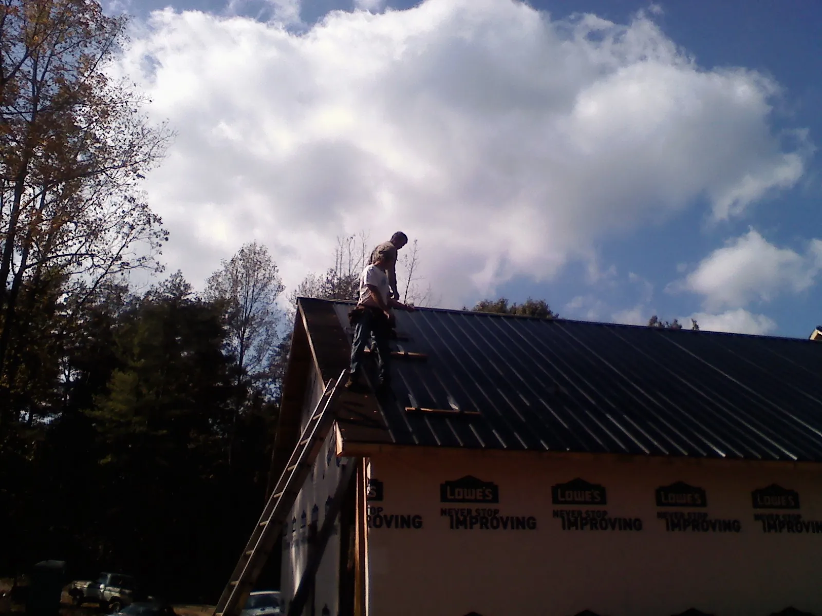 Roofer fastening dark metal panels high against a cloudy sky, from a Roof Inspection job in Jacksonboro