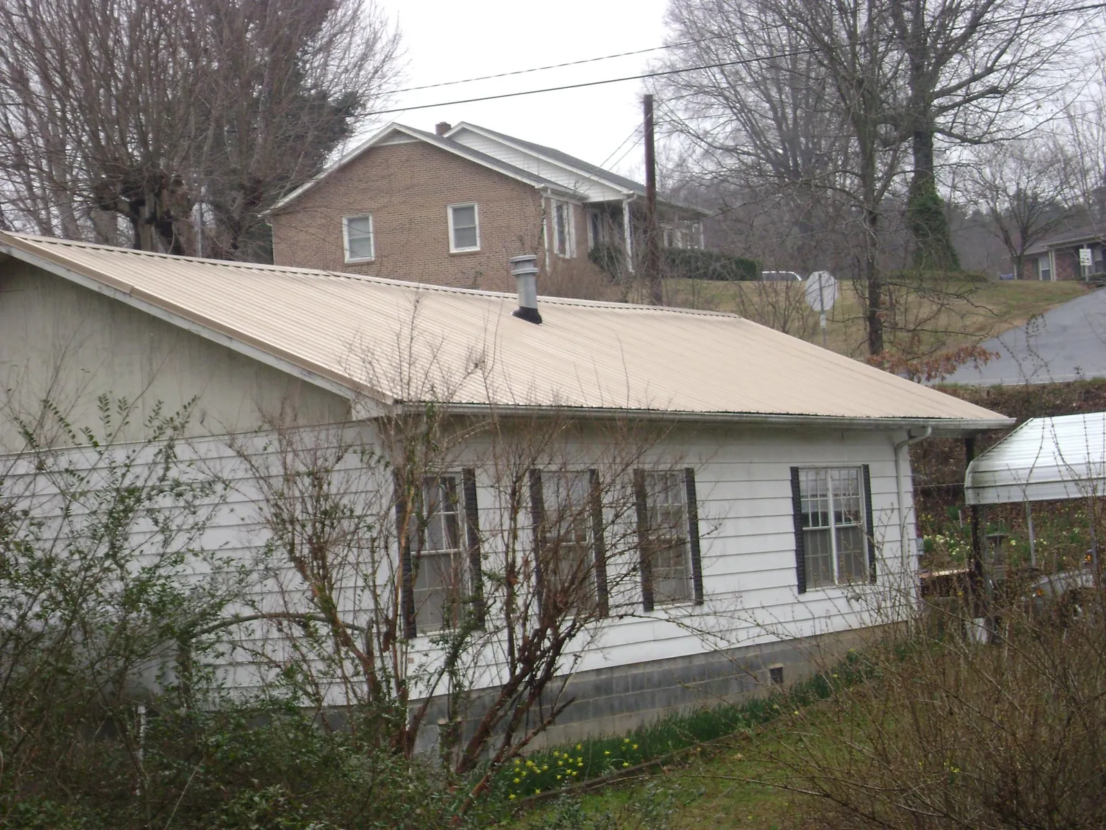 Tan metal roof on a white sided house set into a hillside — Commercial Roofing by Roofing Brothers in Jacksonboro